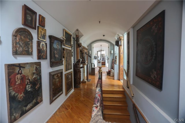 corridor featuring light wood-type flooring, vaulted ceiling, a chandelier, and a wealth of natural light