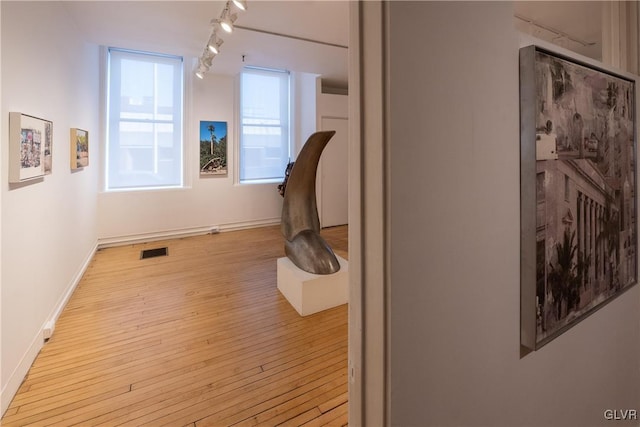 hall with track lighting, light wood-style floors, baseboards, and visible vents