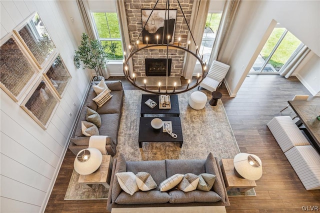 living room with an inviting chandelier, a high ceiling, a brick fireplace, and hardwood / wood-style floors