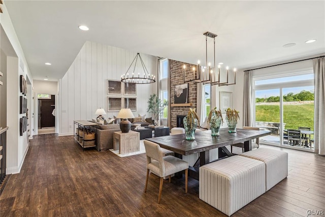 dining space with an inviting chandelier, brick wall, dark wood-type flooring, and a brick fireplace