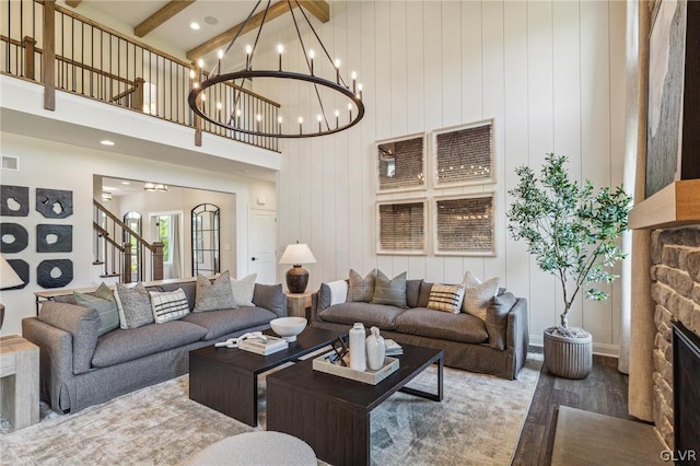 living room with a fireplace, a high ceiling, beam ceiling, a chandelier, and wood-type flooring