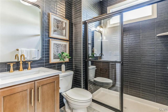 bathroom featuring tile walls, a shower with shower door, toilet, and vanity