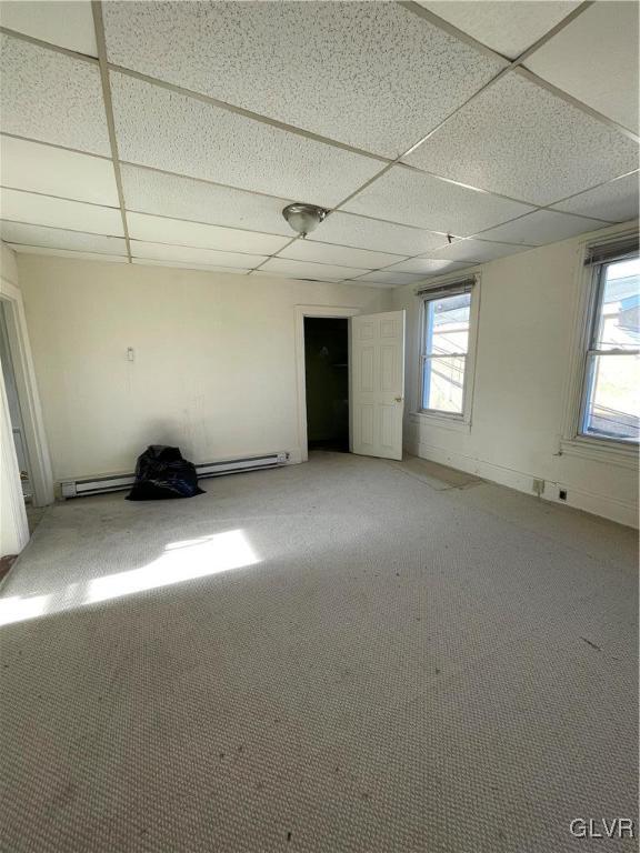 interior space with a baseboard heating unit, a wealth of natural light, and a paneled ceiling