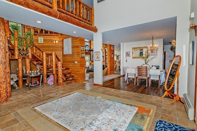 living area with stairway, a chandelier, a high ceiling, wooden walls, and stone tile flooring