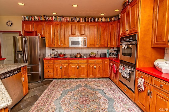 kitchen featuring light stone counters, stainless steel appliances, tasteful backsplash, and dark tile patterned flooring