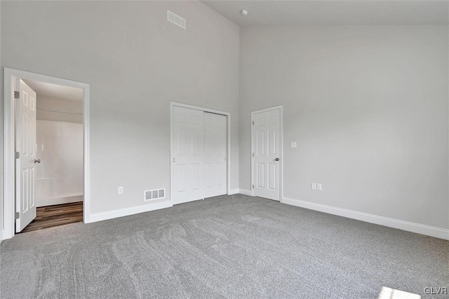 unfurnished bedroom with carpet, a closet, and high vaulted ceiling