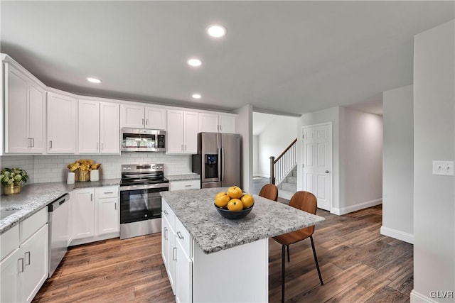 kitchen featuring hardwood / wood-style floors, decorative backsplash, a kitchen island, stainless steel appliances, and white cabinets