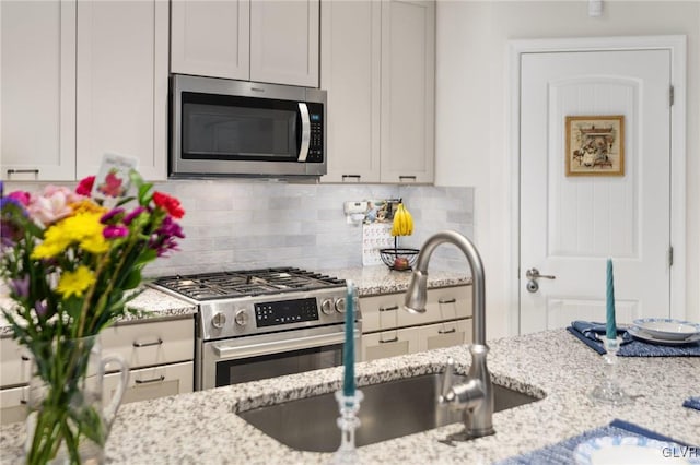 kitchen with backsplash, sink, light stone countertops, and appliances with stainless steel finishes