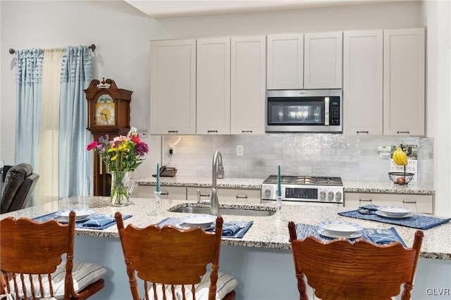 kitchen with white cabinets, appliances with stainless steel finishes, light stone counters, sink, and a kitchen bar