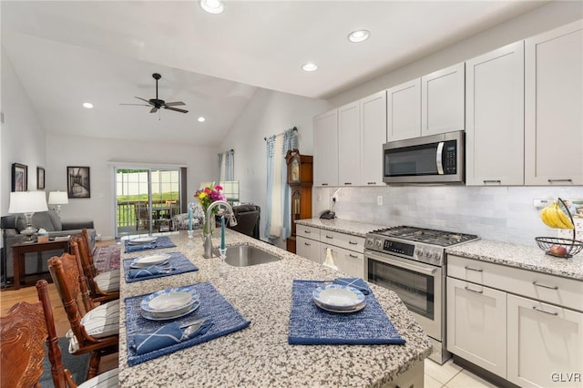 kitchen with appliances with stainless steel finishes, vaulted ceiling, light stone counters, and sink