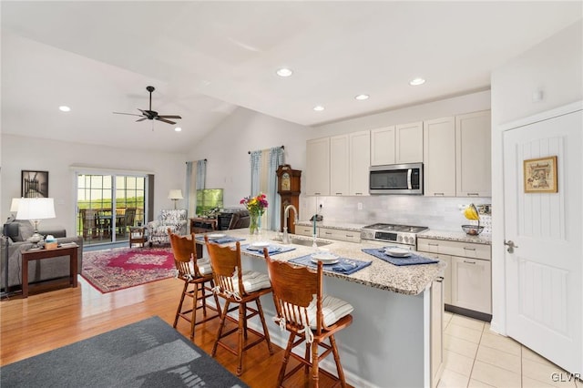 kitchen with light hardwood / wood-style flooring, appliances with stainless steel finishes, ceiling fan, lofted ceiling, and a breakfast bar area