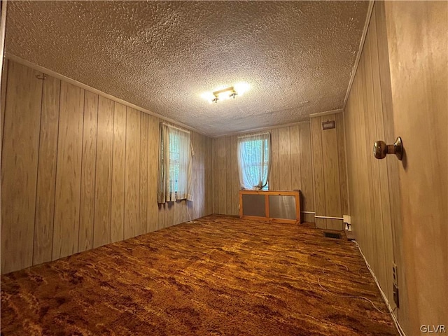 unfurnished room with wooden walls, a textured ceiling, and carpet floors