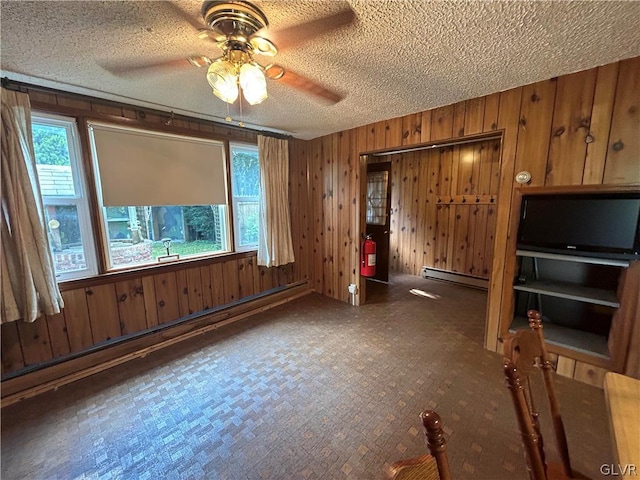 unfurnished living room with a textured ceiling, ceiling fan, wooden walls, and baseboard heating