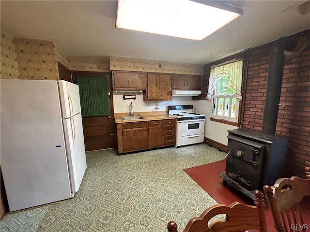 kitchen with white appliances, light tile patterned flooring, sink, and a wood stove