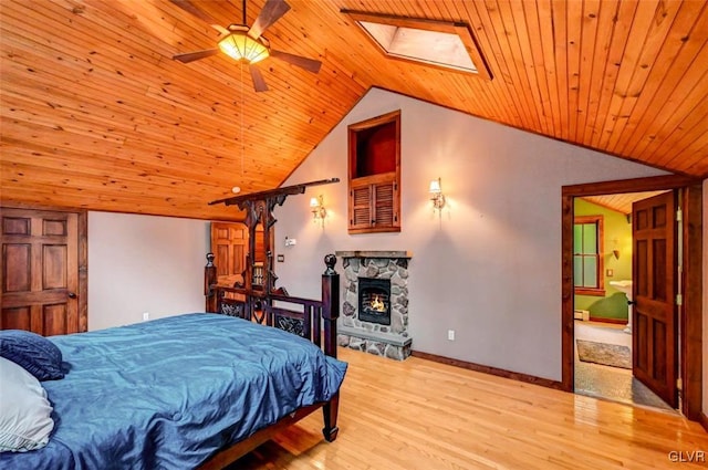 bedroom with a stone fireplace, wood ceiling, vaulted ceiling with skylight, light wood-type flooring, and ceiling fan