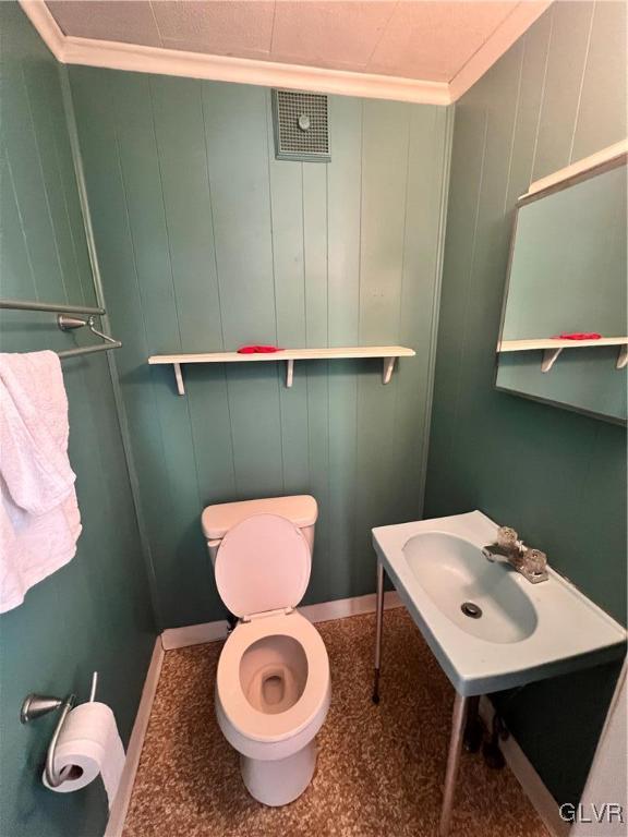 bathroom featuring wood walls, toilet, ornamental molding, and sink