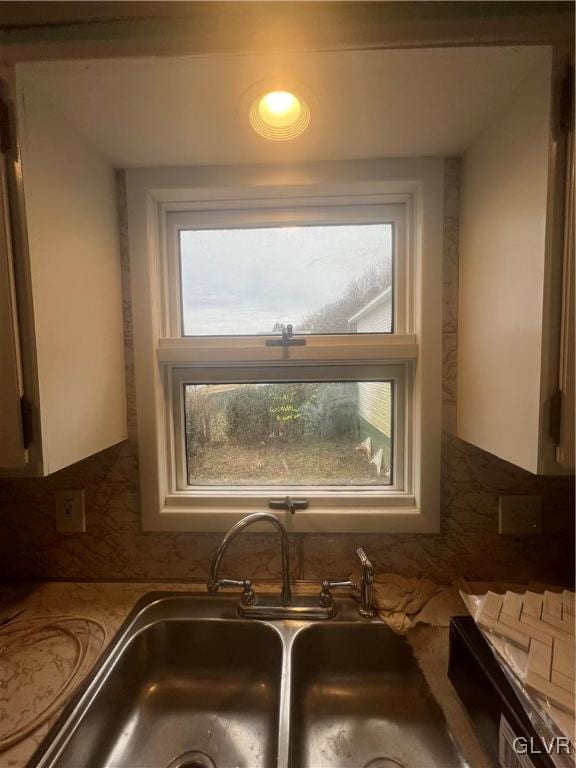 interior details featuring backsplash, dark stone countertops, white cabinetry, and sink