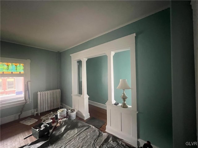 bedroom with decorative columns, crown molding, radiator heating unit, and wood-type flooring