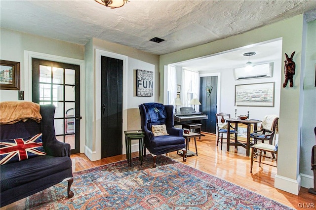 living area with a wall mounted AC, a textured ceiling, and light wood-type flooring