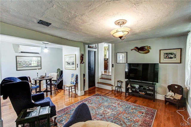 living room with an AC wall unit, a textured ceiling, and hardwood / wood-style flooring