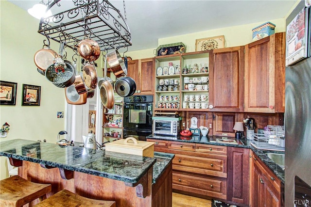 kitchen with dark stone countertops, double oven, light hardwood / wood-style floors, and a breakfast bar