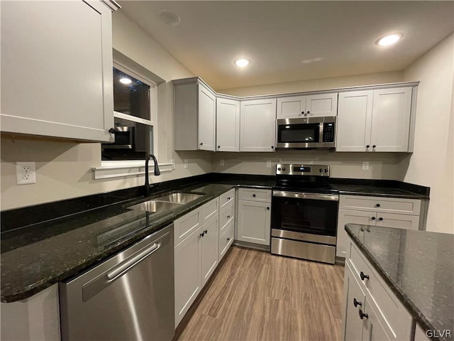 kitchen with dark stone counters, appliances with stainless steel finishes, sink, and light wood-type flooring