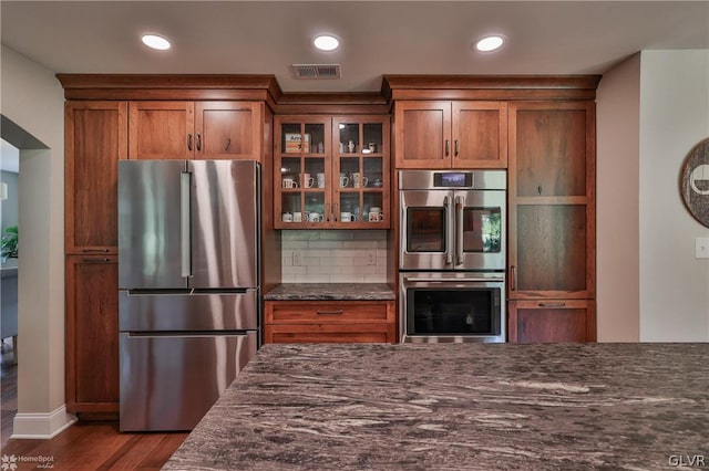 kitchen featuring decorative backsplash, appliances with stainless steel finishes, dark hardwood / wood-style floors, and dark stone counters