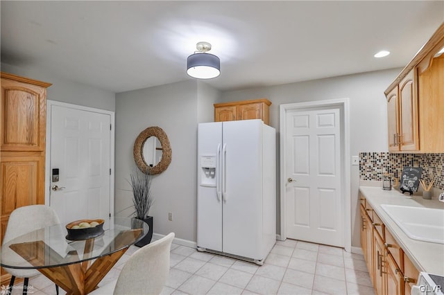 kitchen featuring decorative backsplash, light tile patterned flooring, sink, and white refrigerator with ice dispenser