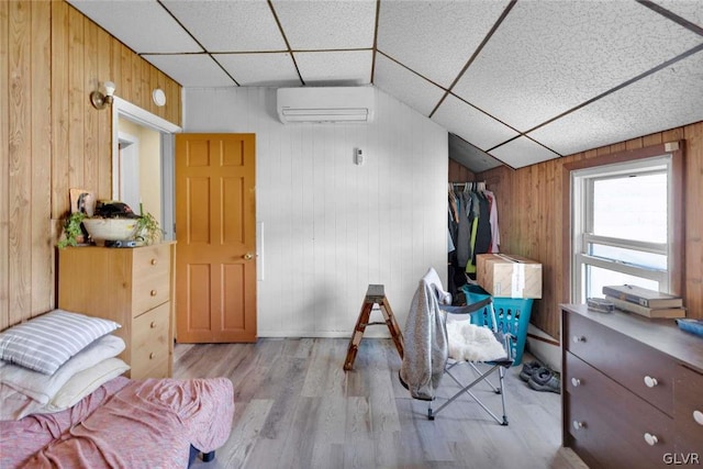 bedroom with wood walls, a drop ceiling, light hardwood / wood-style flooring, and a wall mounted air conditioner