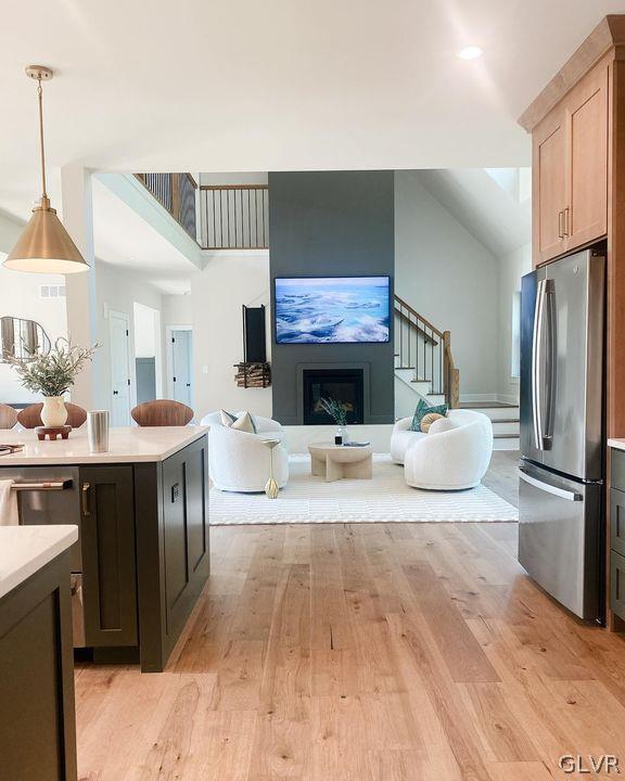 kitchen featuring stainless steel fridge, light hardwood / wood-style flooring, decorative light fixtures, light brown cabinetry, and lofted ceiling