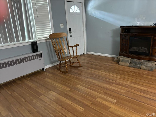 foyer featuring a stone fireplace, wood-type flooring, and radiator heating unit