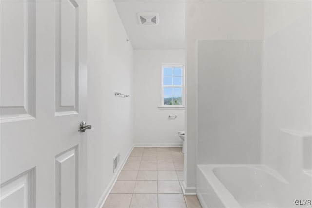 bathroom featuring tile patterned flooring, toilet, and a tub to relax in