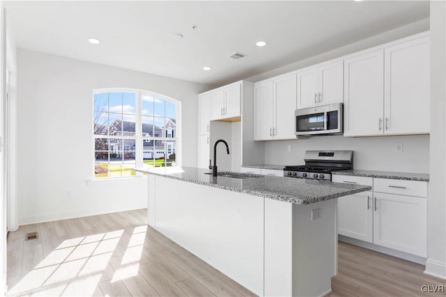 kitchen with sink, stainless steel appliances, a center island with sink, white cabinets, and light wood-type flooring