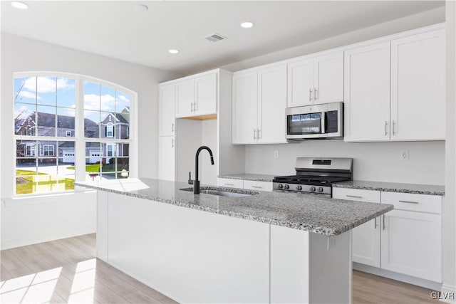 kitchen with a kitchen island with sink, sink, light hardwood / wood-style floors, white cabinetry, and stainless steel appliances