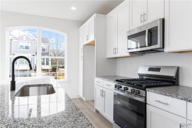 kitchen with white cabinetry, sink, stainless steel appliances, light stone counters, and light wood-type flooring