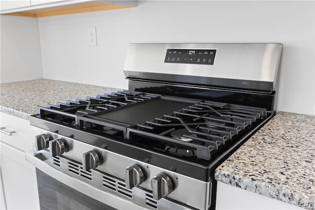 interior details featuring stainless steel gas stove, light stone countertops, and white cabinetry