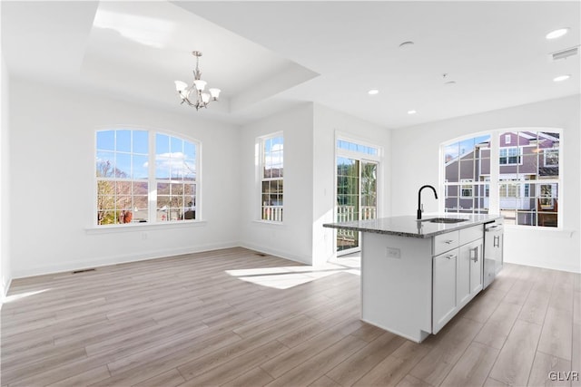 kitchen featuring sink, light hardwood / wood-style floors, dark stone counters, and an island with sink