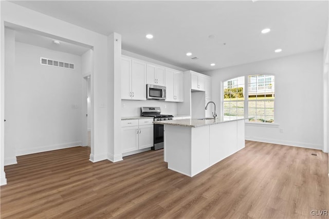 kitchen featuring white cabinets, stainless steel appliances, light hardwood / wood-style flooring, and an island with sink