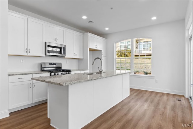 kitchen with an island with sink, stainless steel appliances, white cabinetry, and sink