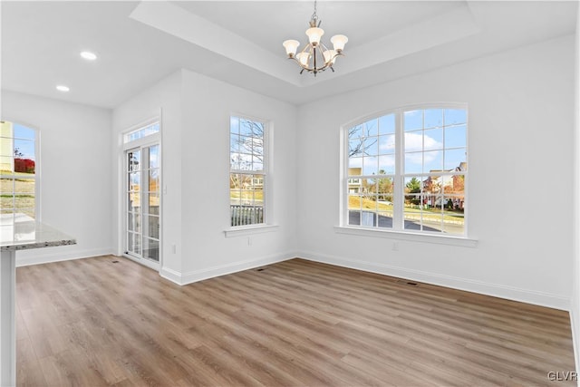 unfurnished dining area featuring hardwood / wood-style flooring, an inviting chandelier, and a wealth of natural light