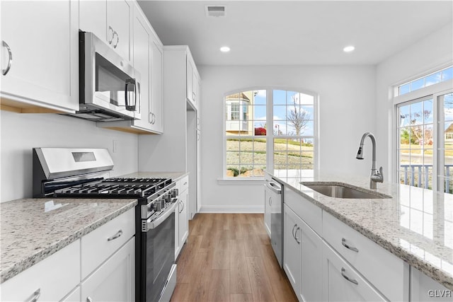 kitchen with light stone countertops, sink, stainless steel appliances, white cabinets, and light wood-type flooring