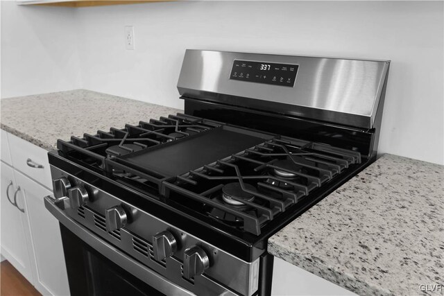 interior details featuring white cabinetry, light stone counters, and stainless steel range with gas cooktop