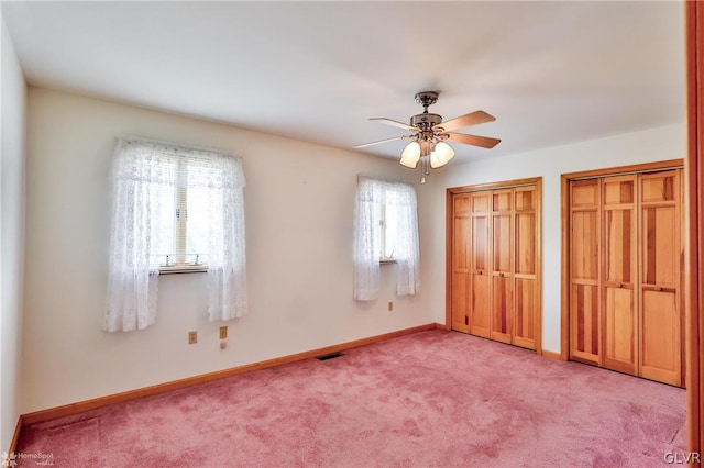 unfurnished bedroom with light carpet, ceiling fan, and two closets