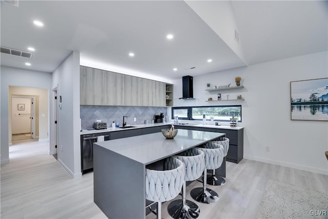 kitchen featuring sink, wall chimney exhaust hood, a center island, a breakfast bar area, and light hardwood / wood-style floors