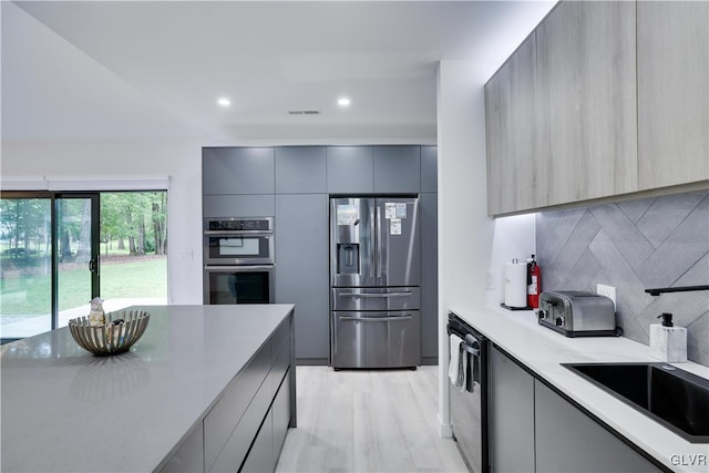 kitchen featuring gray cabinetry, stainless steel appliances, decorative backsplash, and light hardwood / wood-style flooring