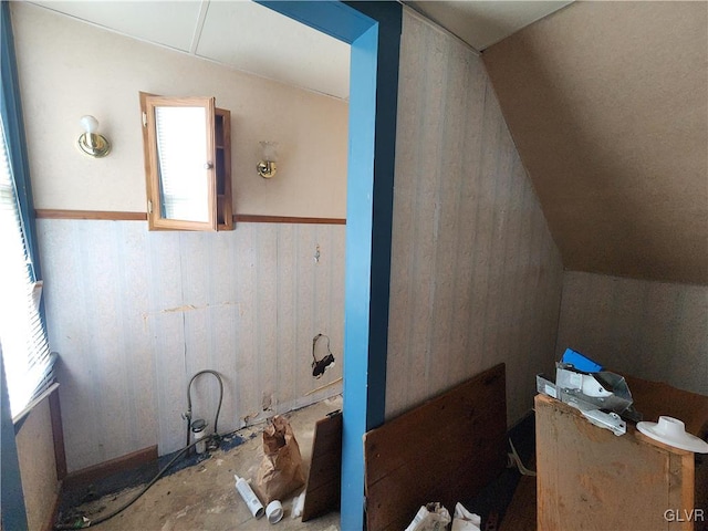 bathroom featuring vaulted ceiling, plenty of natural light, and wooden walls