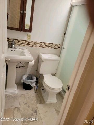 bathroom featuring toilet, tasteful backsplash, tile patterned flooring, and tile walls