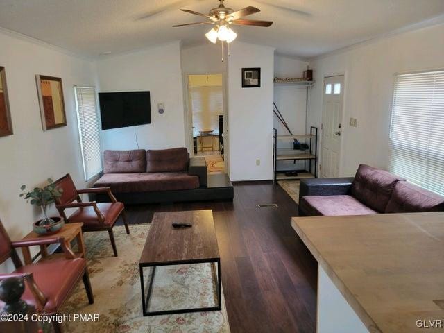 living room with crown molding, ceiling fan, wood-type flooring, and a healthy amount of sunlight