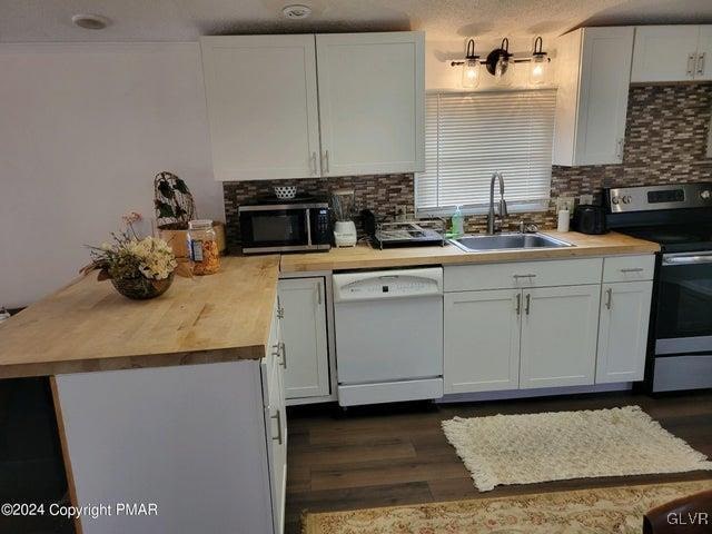 kitchen with white cabinetry, butcher block counters, backsplash, stainless steel appliances, and sink