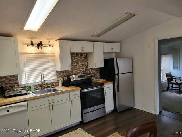 kitchen featuring appliances with stainless steel finishes, sink, backsplash, white cabinetry, and dark wood-type flooring